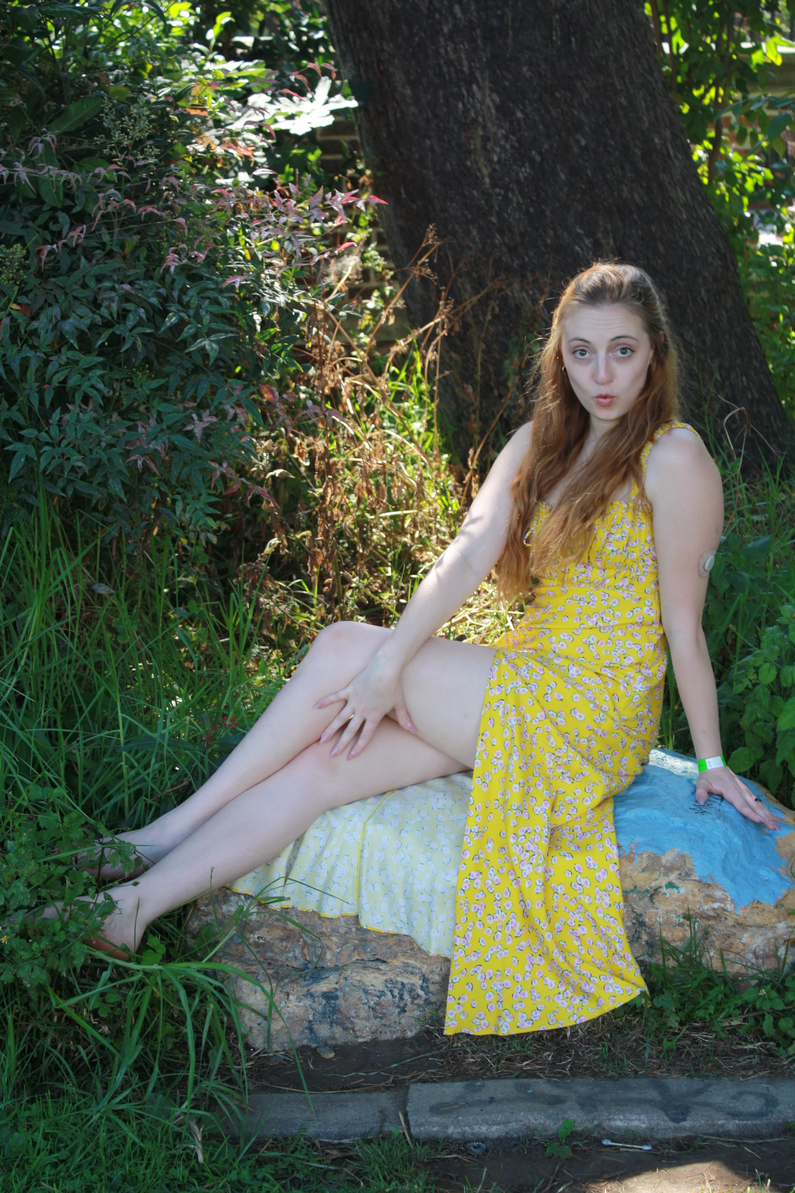 Jordie Morris sitting sideways on a blue-painted rock beneath a tree at the Exposition Park Rose Garden.